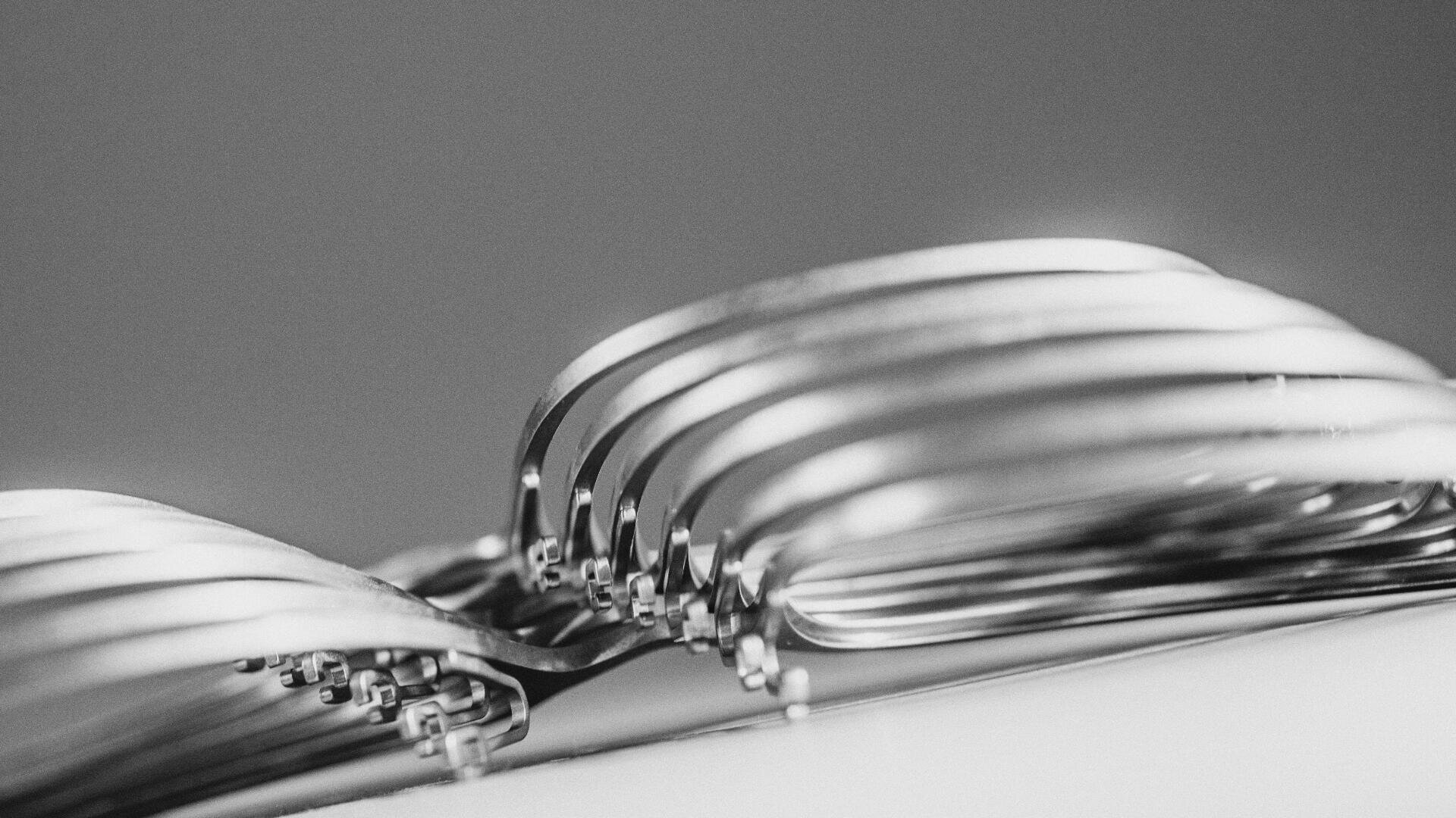 Eine Nahaufnahme in Schwarzweiß von mehreren übereinander gestapelten Metallgabeln, wobei der Schwerpunkt auf den gebogenen Zinken liegt und ein abstraktes, symmetrisches Muster mit einem weichen, unscharfen Hintergrund entsteht.
