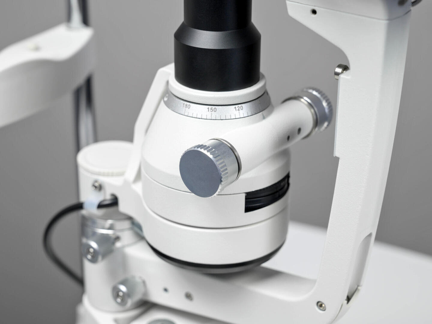 Nahaufnahme eines weiß-schwarzen ophthalmischen Spaltlampenmikroskops für Augenuntersuchungen. Zu sehen sind Einstellknöpfe und ein Teil des Linsensystems.