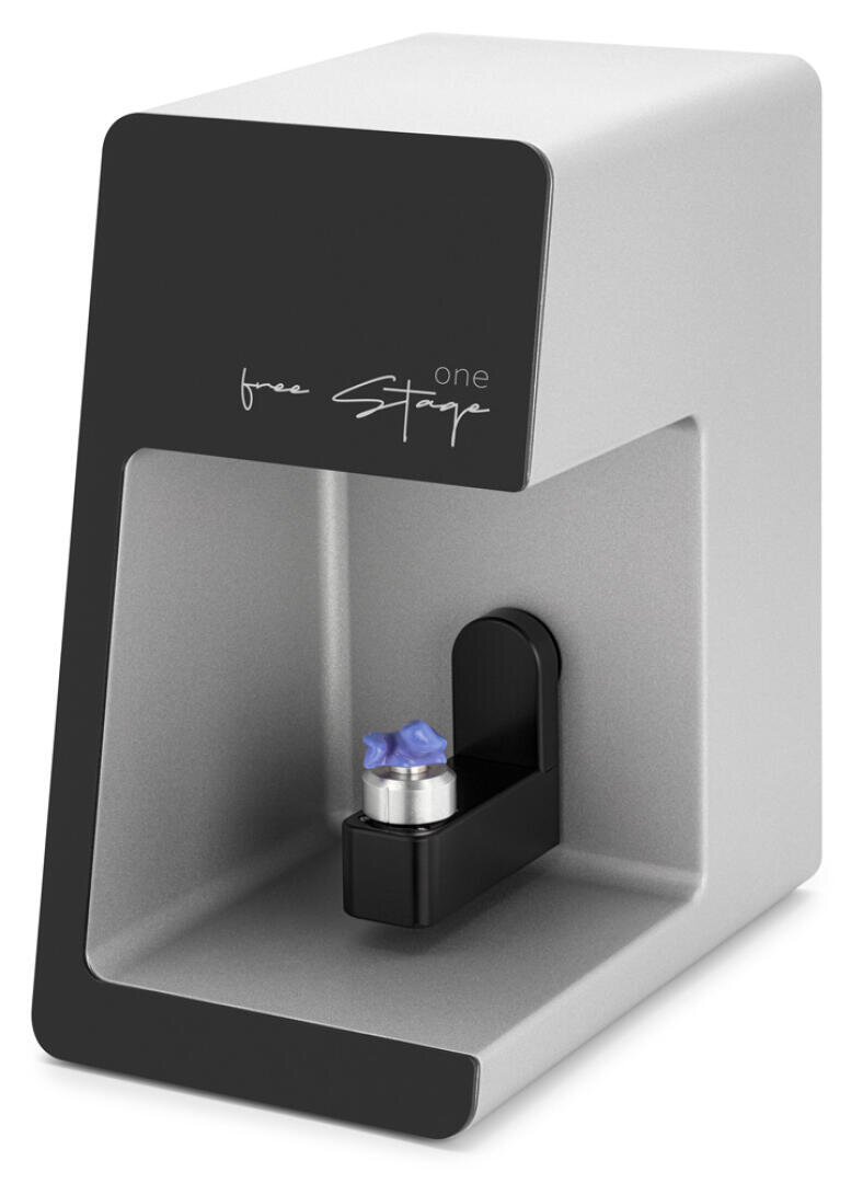 A compact, modern desktop device with a metal gray housing and a black front panel with the text free Stage one. The device holds a small object, possibly dental equipment, on its platform.