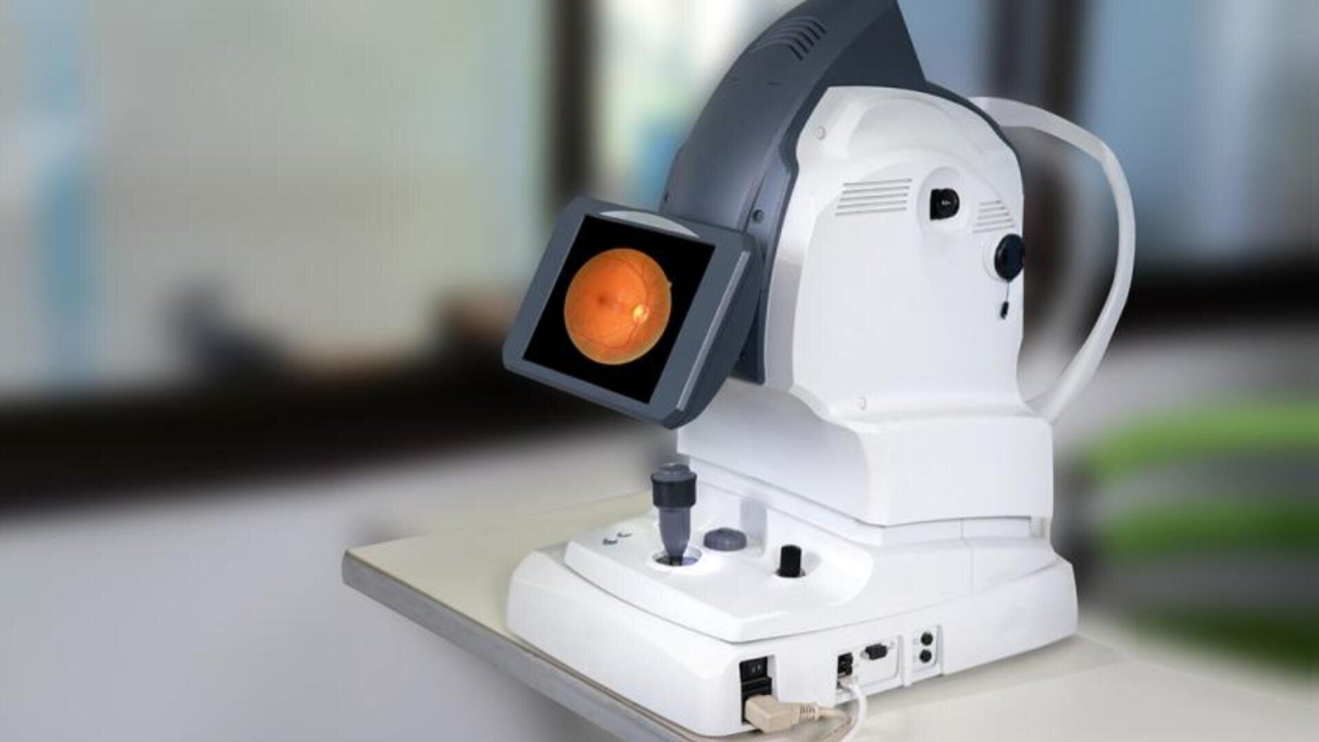 Auf einem Tisch steht ein Gerät zur Netzhautbildgebung. Auf seinem Bildschirm wird eine Nahaufnahme der menschlichen Netzhaut angezeigt. Das Gerät verfügt über verschiedene Knöpfe, Regler und Anschlüsse. Der Hintergrund ist unscharf.