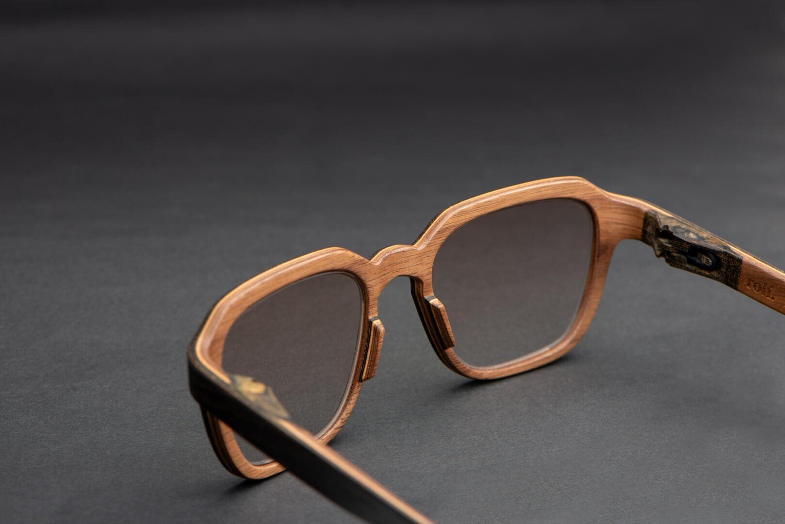 Close-up of stylish wooden sunglasses with dark lenses, placed on a dark surface, showcasing the frame details and subtle wood grain texture.