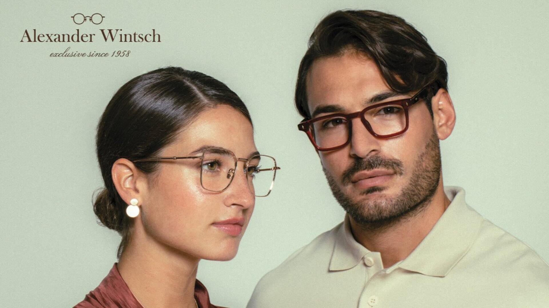 A woman and a man wearing stylish eyeglasses pose against a light background. The woman has her hair back and wears gold-framed glasses; the man has short hair, facial hair, and wears brown glasses. Alexander Wintsch logo is in the corner.