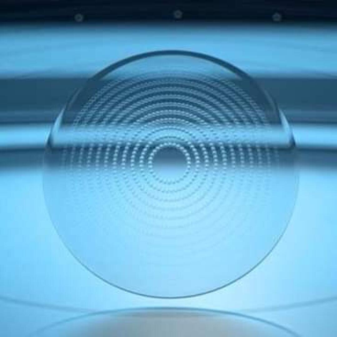 Eine transparente kreisförmige Linse mit konzentrischen gepunkteten Ringen schwebt vor einem blauen Hintergrund mit Farbverlauf und erzeugt einen futuristischen und symmetrischen optischen Effekt.
