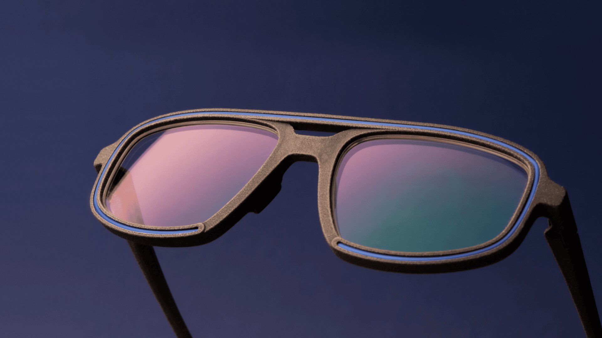 Nahaufnahme einer stilvollen Sonnenbrille mit schwarzem Rahmen und reflektierenden rosa-grünen Gläsern vor einem dunkelblauen Hintergrund.