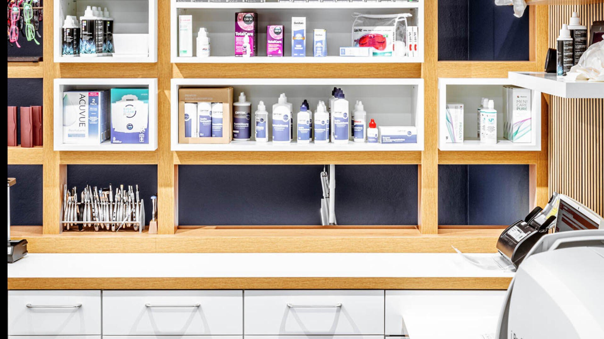 Ein modernes Apothekenregal mit verschiedenen Flaschen, Schachteln und medizinischen Vorräten, ordentlich angeordnet in offenen Holzfächern über einer weißen Theke mit Schubladen.