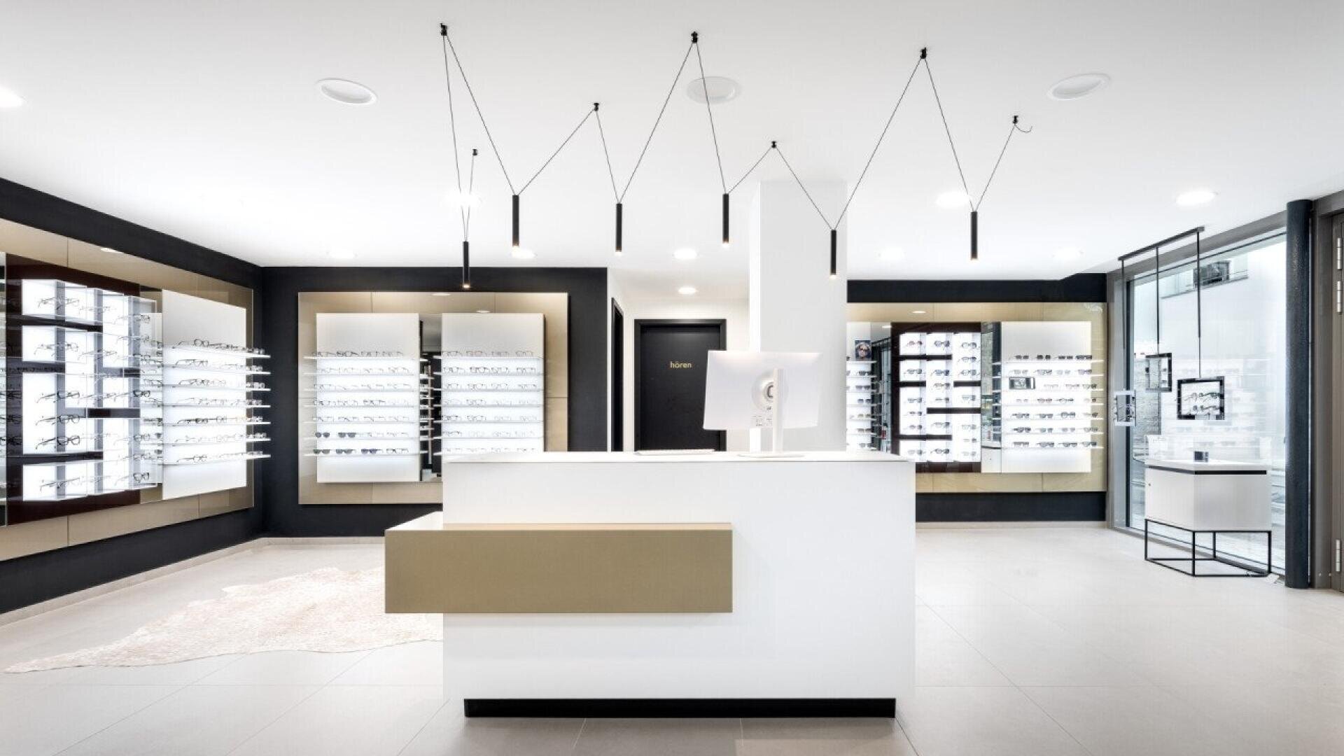 A modern optician’s store interior with a white counter, display shelves filled with eyeglasses on the walls, minimalist lighting, and a clean, bright atmosphere.