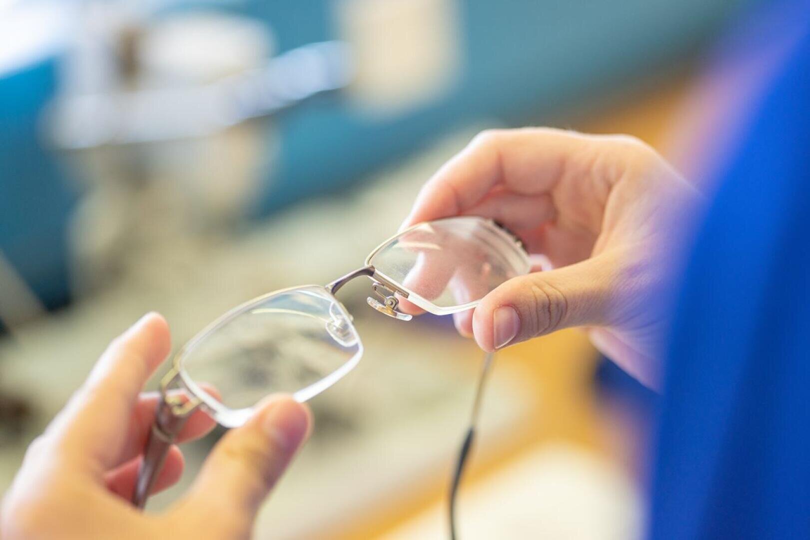 Eine Person hält eine Brille mit beiden Händen und prüft die Gläser genau. Der Hintergrund ist leicht unscharf und lenkt die Aufmerksamkeit auf die Brille und die Hände.