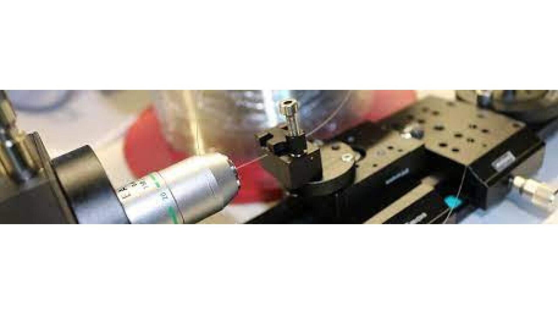 Close-up view of scientific laboratory equipment, including a microscope lens and precision instruments, used for detailed examination or manipulation of small samples or components.