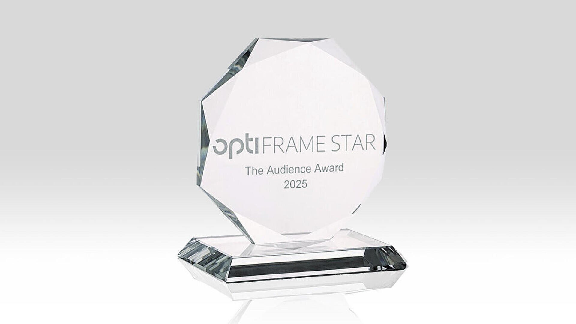 Ein klarer, facettierter Glaspreis mit der Aufschrift „optiFRAME STAR The Audience Award 2025“, stehend auf einem passenden Glassockel vor hellgrauem Hintergrund.