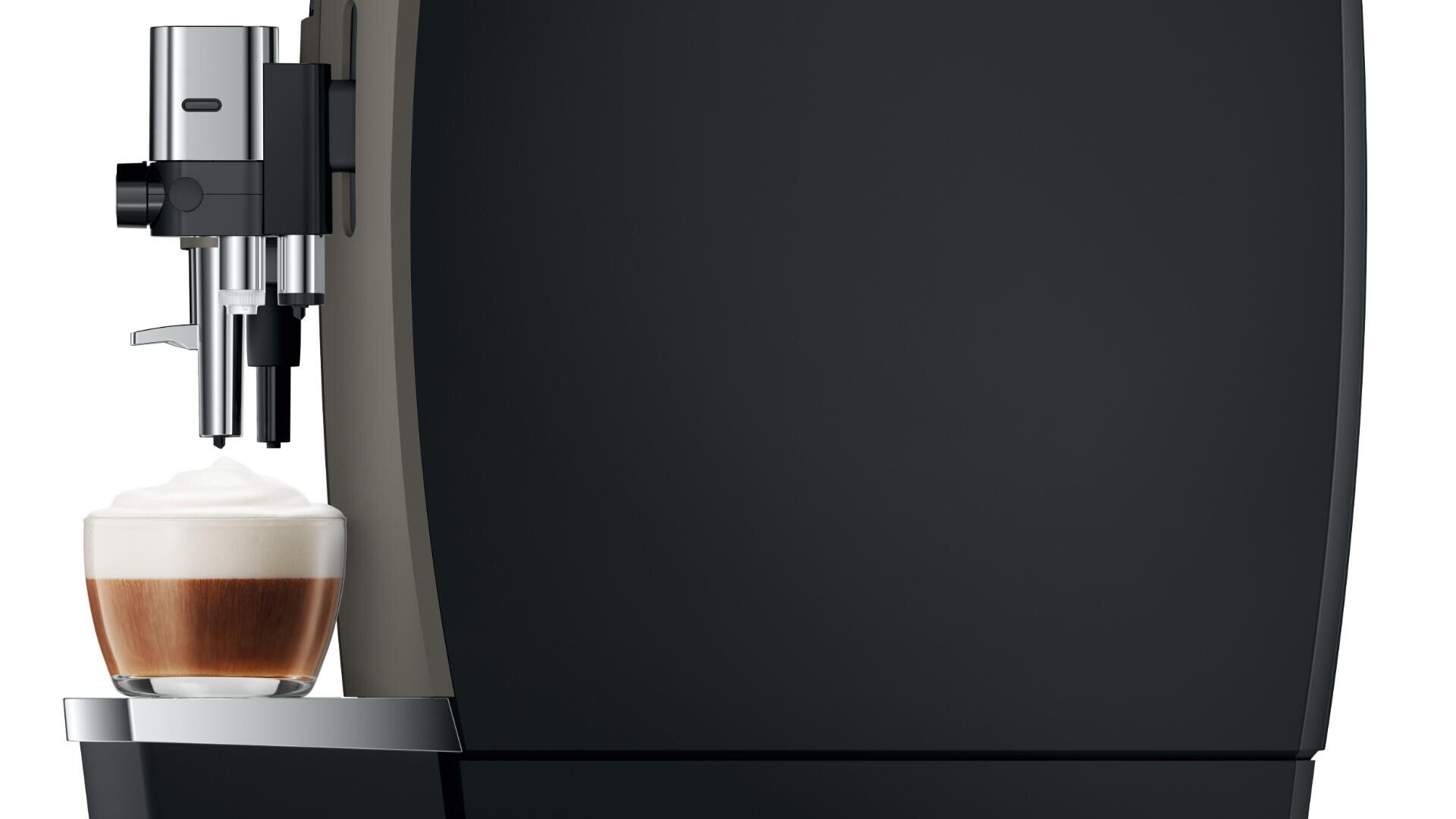 Eine Nahaufnahme einer modernen schwarzen Kaffeemaschine, die einen Cappuccino mit aufgeschäumter Milch in eine Glastasse ausgibt, ist auf der linken Seite des Bildes vor einem dunklen Hintergrund zu sehen.