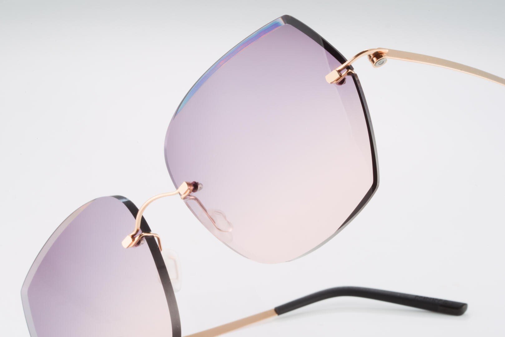 Close-up of stylish sunglasses with large, square, purple lenses with a color gradient and thin golden metal frames against a plain white background.