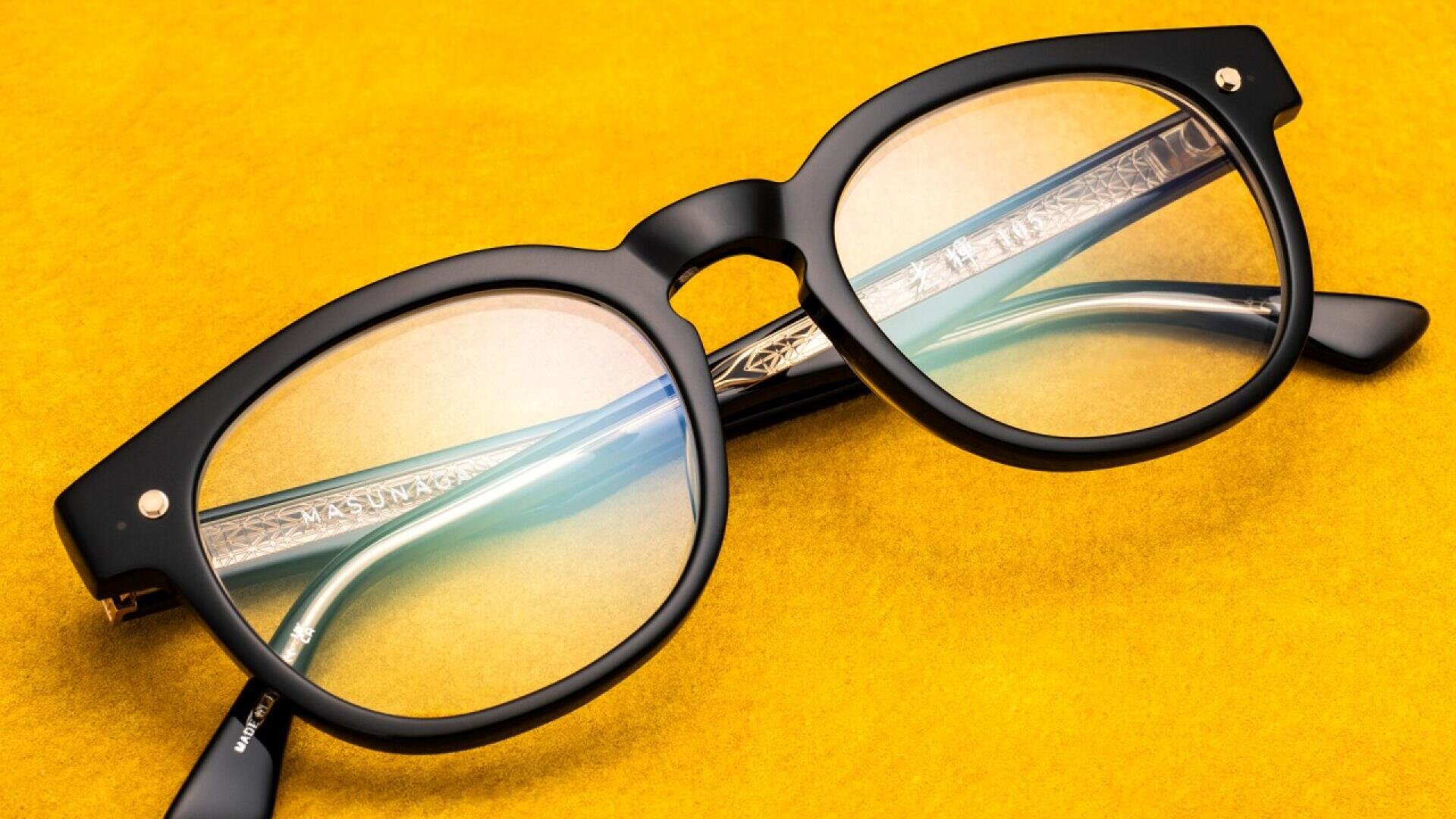 A pair of black-rimmed eyeglasses with slightly tinted lenses lies on a bright yellow surface.