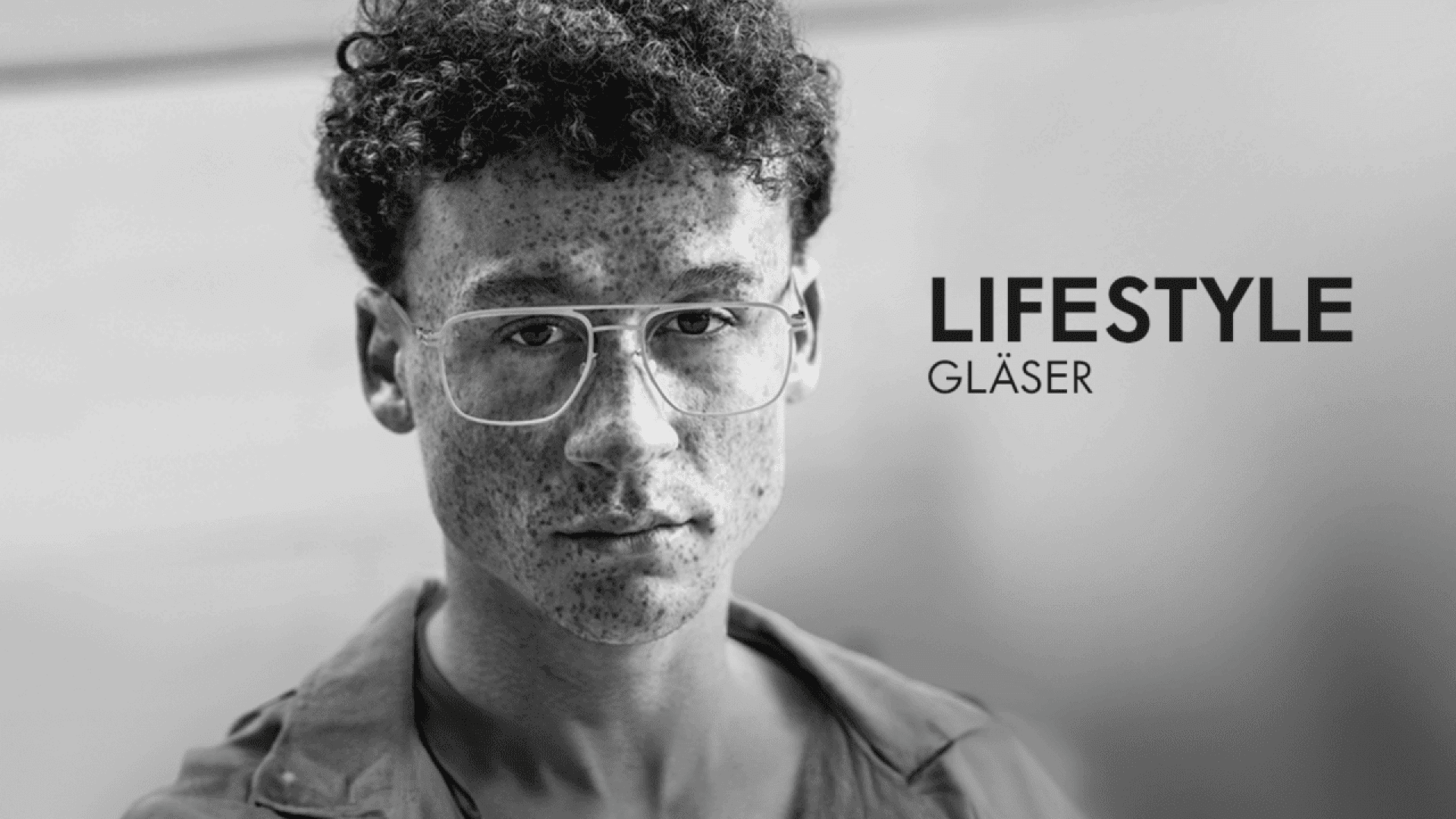 Black and white photo of a person with curly hair, freckles, and large eyeglasses, looking at the camera. The words LIFESTYLE GLÄSER appear in bold on the right side of the image.