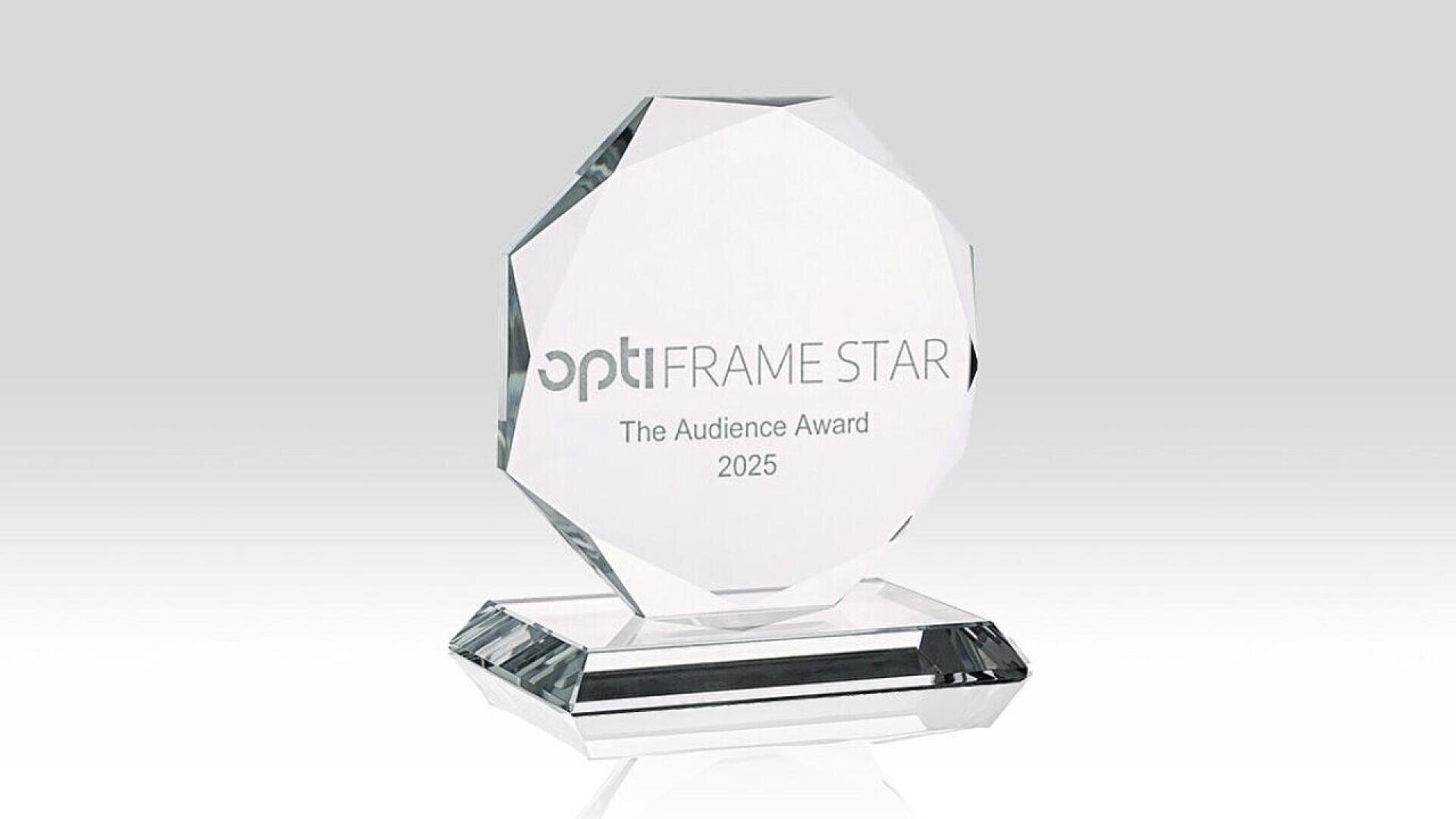 A clear crystal award with the text optiFRAME STAR The Audience Award 2025 engraved on it, standing on a faceted base against a light gray background.