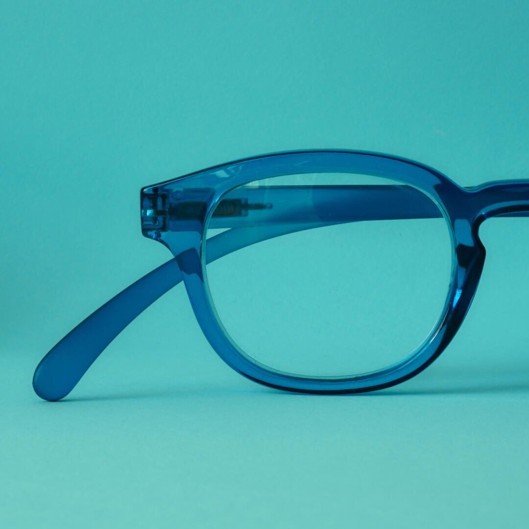 Nahaufnahme der linken Hälfte einer blauen Brille mit transparentem Rahmen vor einem passenden blauen Hintergrund.