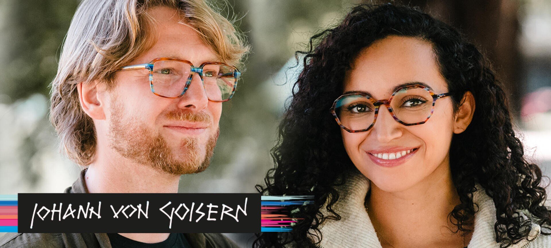 Ein Mann und eine Frau mit bunten Brillen lächeln im Freien. Der Mann hat helles Haar und einen Bart, die Frau dunkles, lockiges Haar. Unten links steht der Text „Johann von Goisern“.