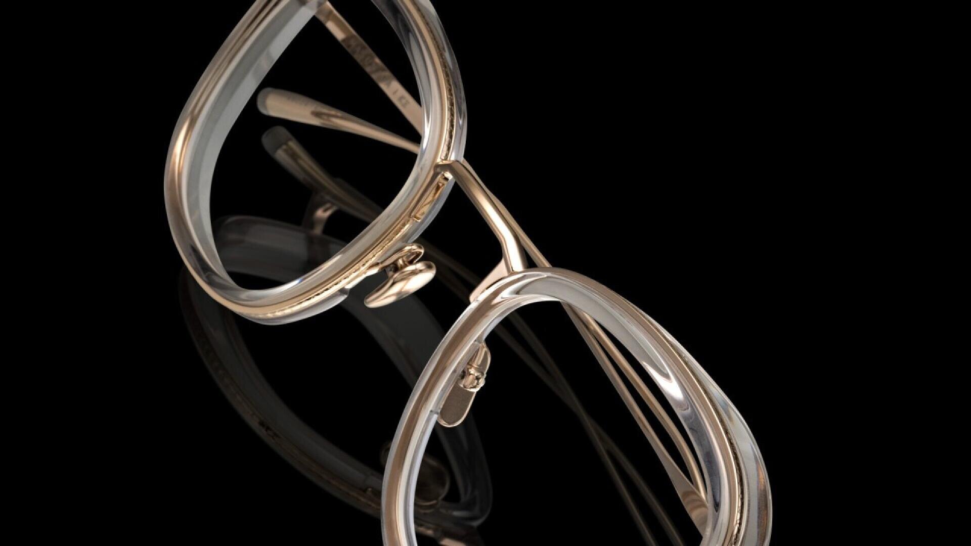A close-up of gold-framed eyeglasses with transparent rims, set against a black background, highlighting the details of the frames and nose pads.