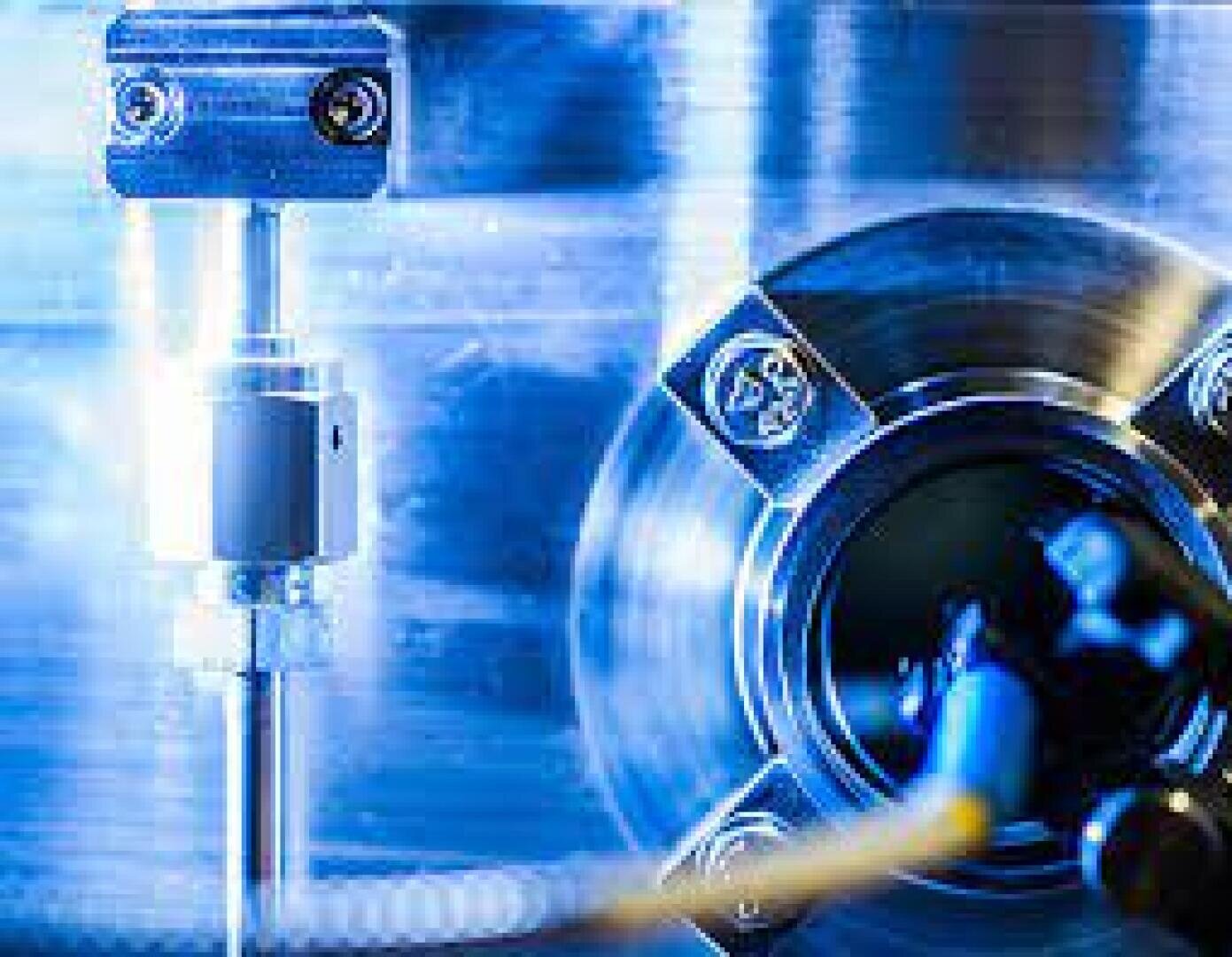 Nahaufnahme von mechanischen Metallteilen mit Schrauben und kreisförmigen Teilen, die mit blauem Licht beleuchtet werden und an Industriemaschinen oder Laborgeräte erinnern.