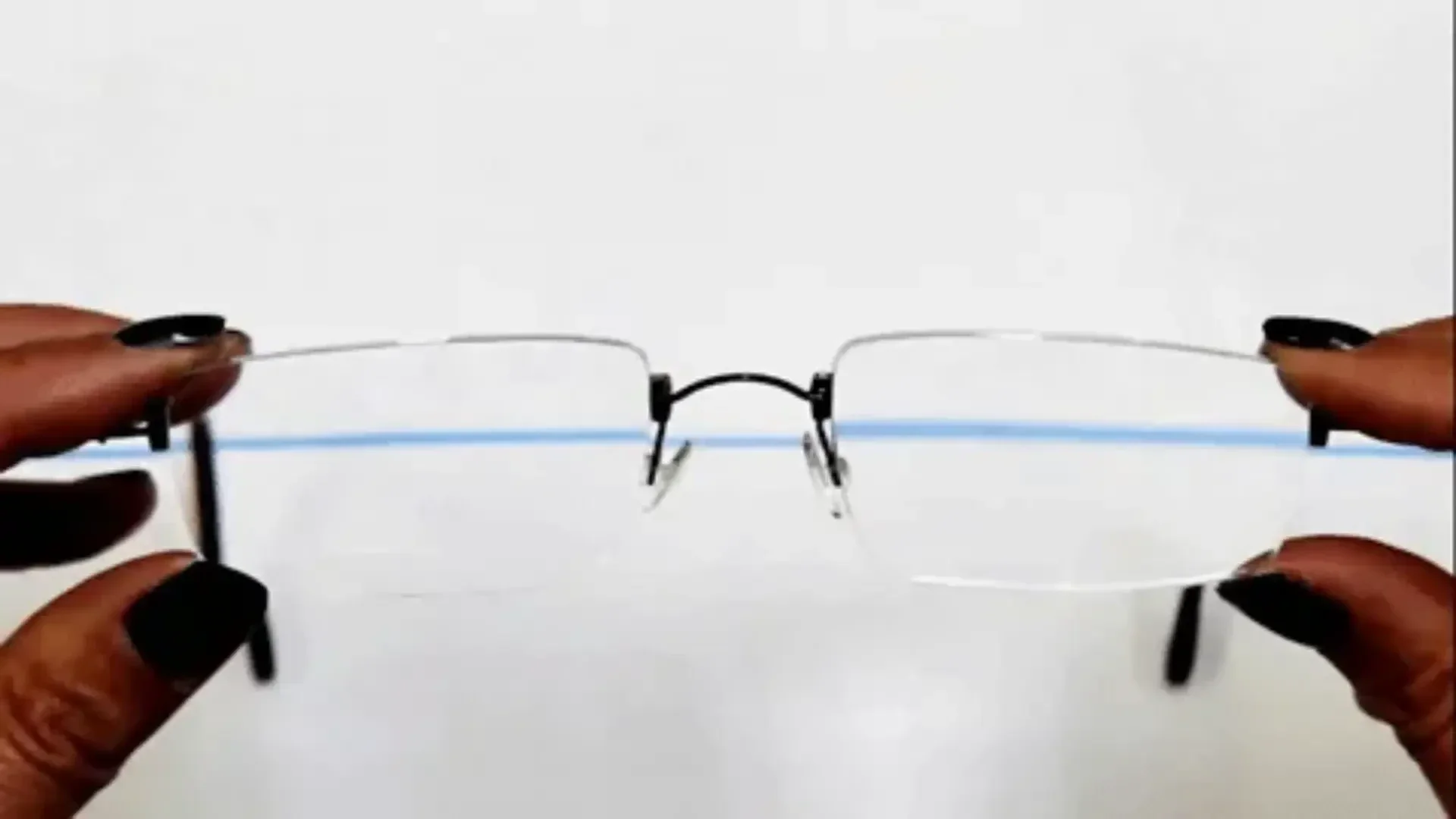 Eine randlose Brille, die mit beiden Händen gehalten wird. Durch die Gläser ist auf weißem Hintergrund eine blaue horizontale Linie sichtbar.