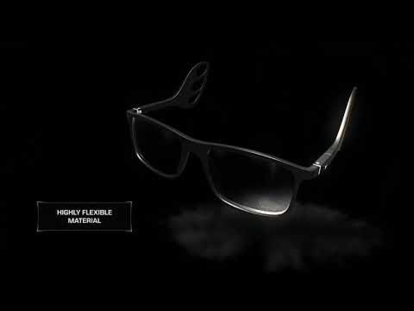 Eine schwarze Brille mit flexiblen Bügeln ist auf einem dunklen Hintergrund abgebildet. Auf einem Etikett im Bild steht "Hochflexibles Material".