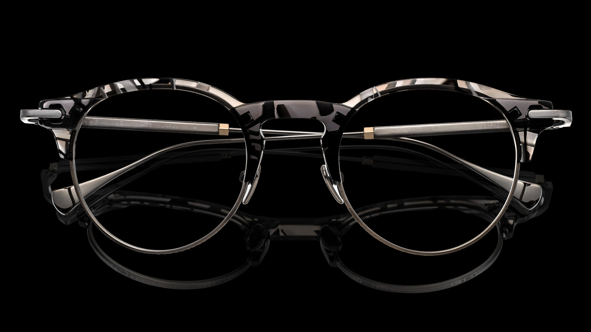 Runde Brille mit schwarz-weiß marmoriertem Rahmen, silbernem Metallsteg und dünnen silbernen Bügeln, die mit geöffneten Bügeln auf schwarzem Hintergrund abgebildet sind.