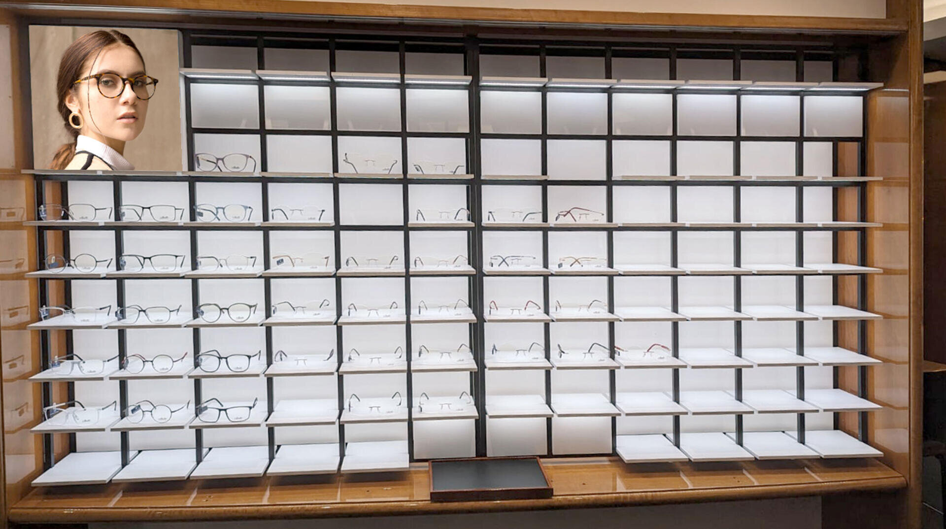 Eine größtenteils leere Auslage mit Brillengestellen in Regalen, von denen nur noch einige wenige übrig sind. In der oberen linken Ecke ist eine Frau mit Brille abgebildet, die zur Seite schaut.