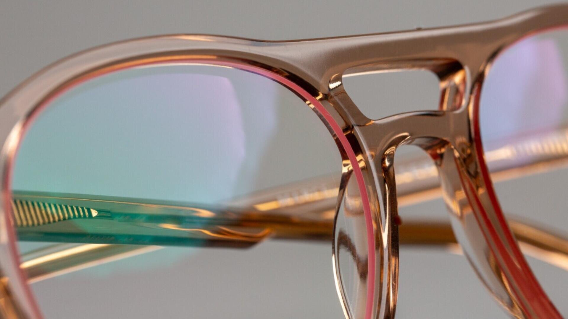 Close-up of stylish, translucent eyeglasses with a gold and pink frame, showing light reflections on the lenses and intricate details of the bridge and arms.