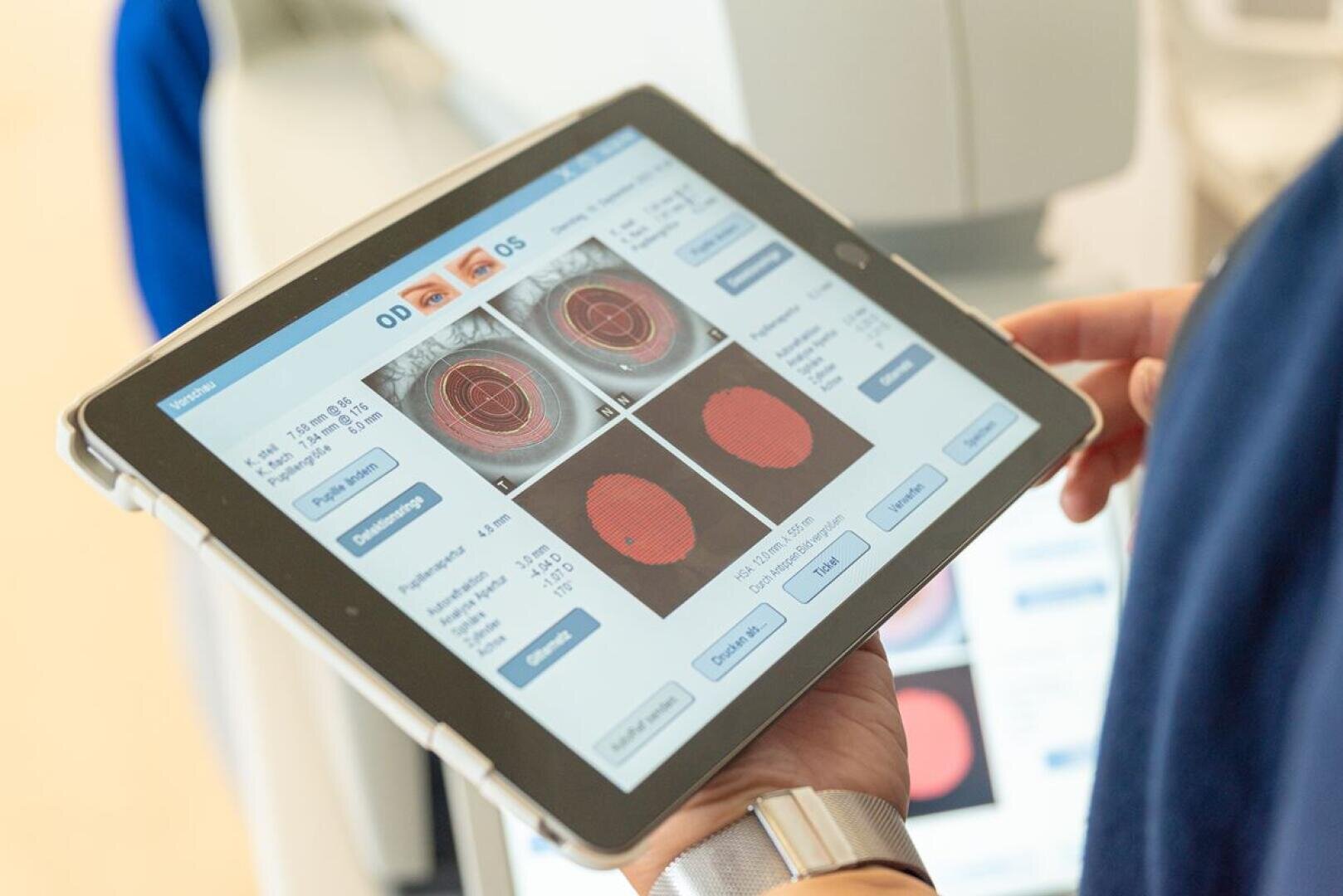 A person is holding a tablet displaying the results of an eye scan with images of the retina and various diagnostic data, probably for an eye examination or vision assessment.