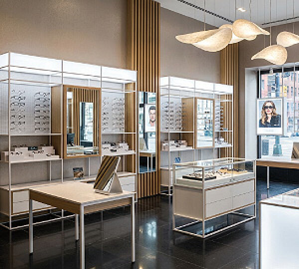 A modern eyewear store with bright lighting, display tables, wall shelves with glasses, large mirrors and modern pendant lights hanging from the ceiling near a window.