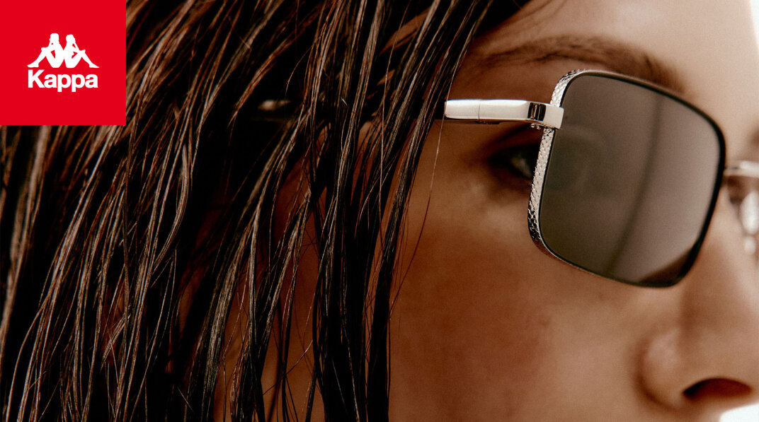 Nahaufnahme des Gesichts einer Person mit quadratischer Sonnenbrille und nassen Haaren. Das Kappa-Logo mit zwei sitzenden Figuren erscheint in der oberen linken Ecke auf rotem Hintergrund.