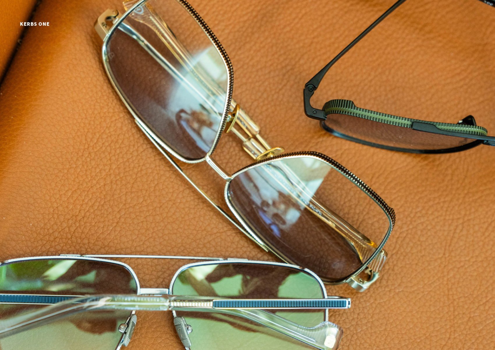 Drei Brillen mit Metallrahmen ruhen auf einer strukturierten braunen Lederoberfläche. Jede Brille hat ein einzigartiges Rahmendesign, und die Gläser spiegeln die Umgebung wider.